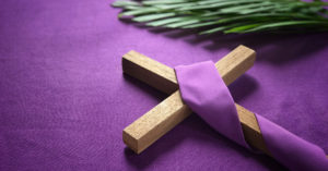 Purple cloth, palm frond, and wooden cross on a table