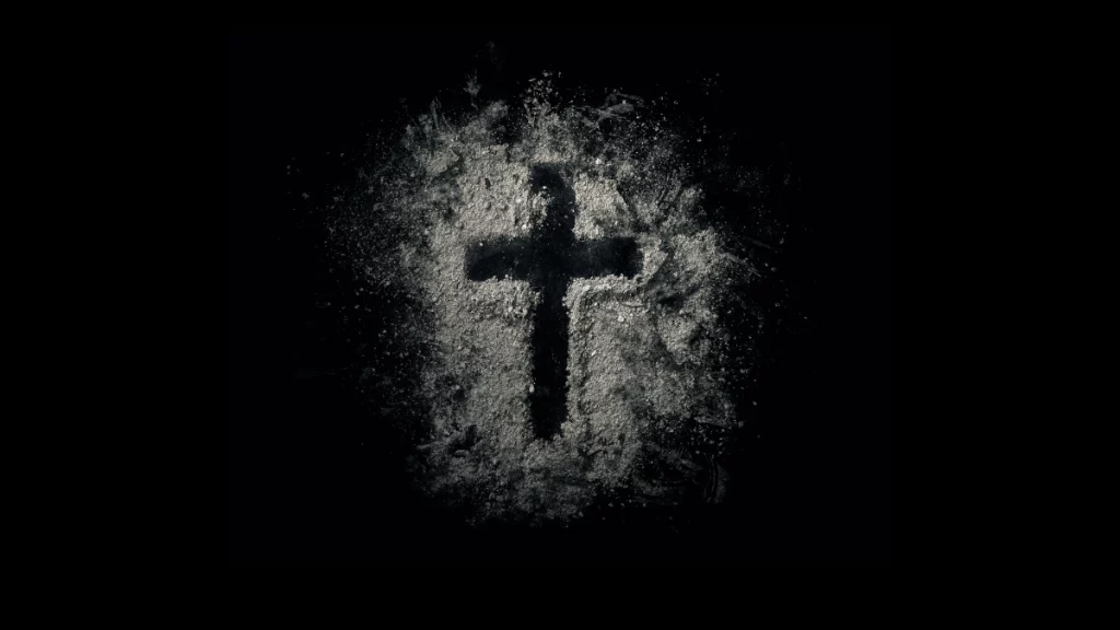 cross drawn on a black background with ashes